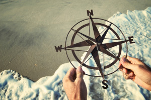Hands Holding Compass Over Waves Rushing on Beach