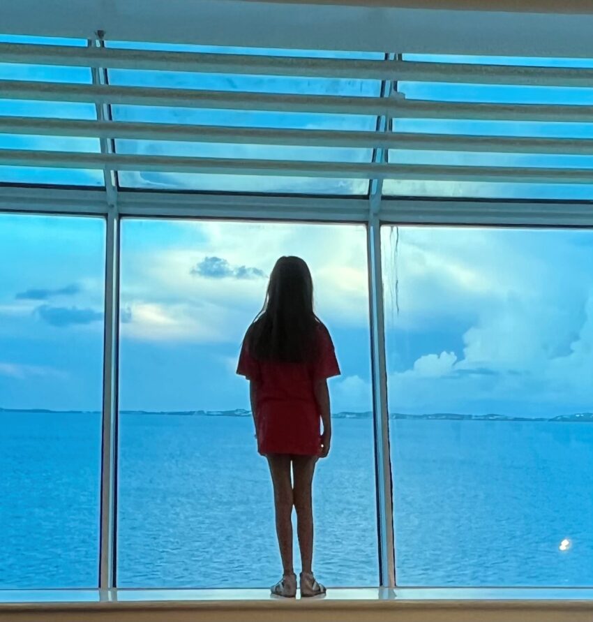 girl standing in front of cruise ship window looking out to ocean