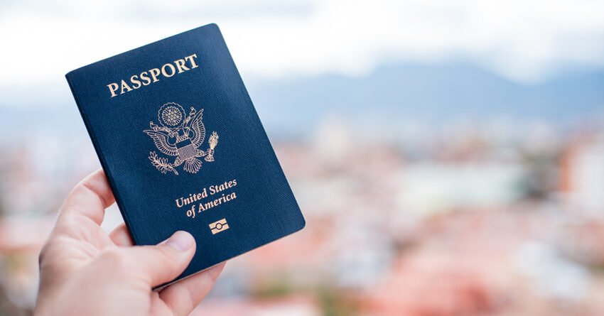 One single hand holding a blue American passport in front of a b