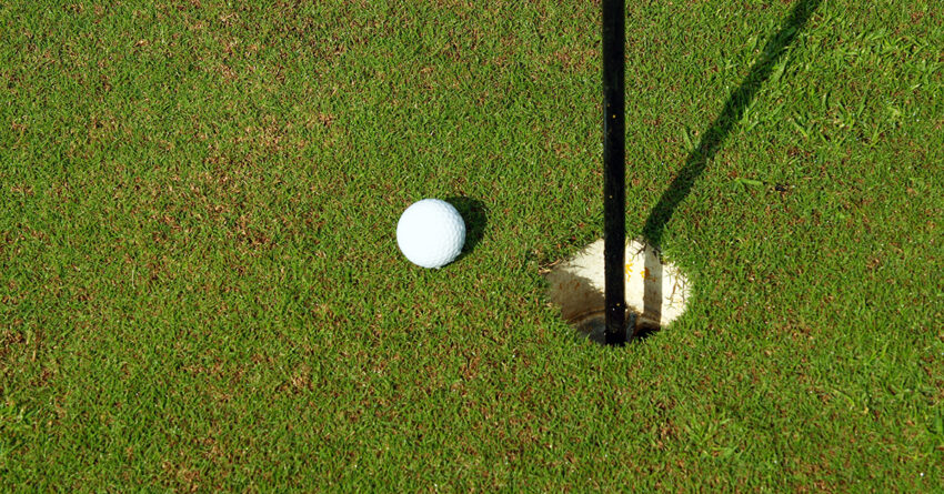 White golf ball near hole on green