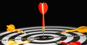 Red dart arrow pining in the target with center of dartboard with yellow dart arrow putting around, competition go-to target and winner-loser business success concept.