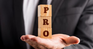 Businessman holding three wooden cubes stacked on the palm of his hand reading a PRO sign. Conceptual of professionalism and success.
